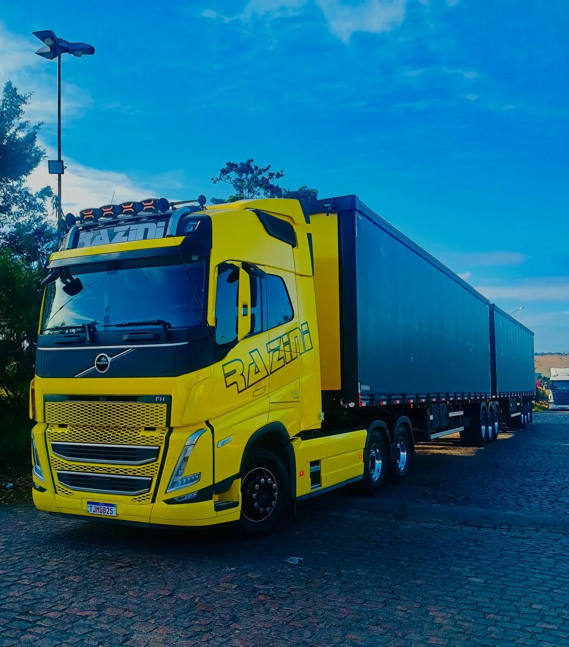 Rodotrem amarelo da Razini, Volvo FH 540, em pátio sob céu azul